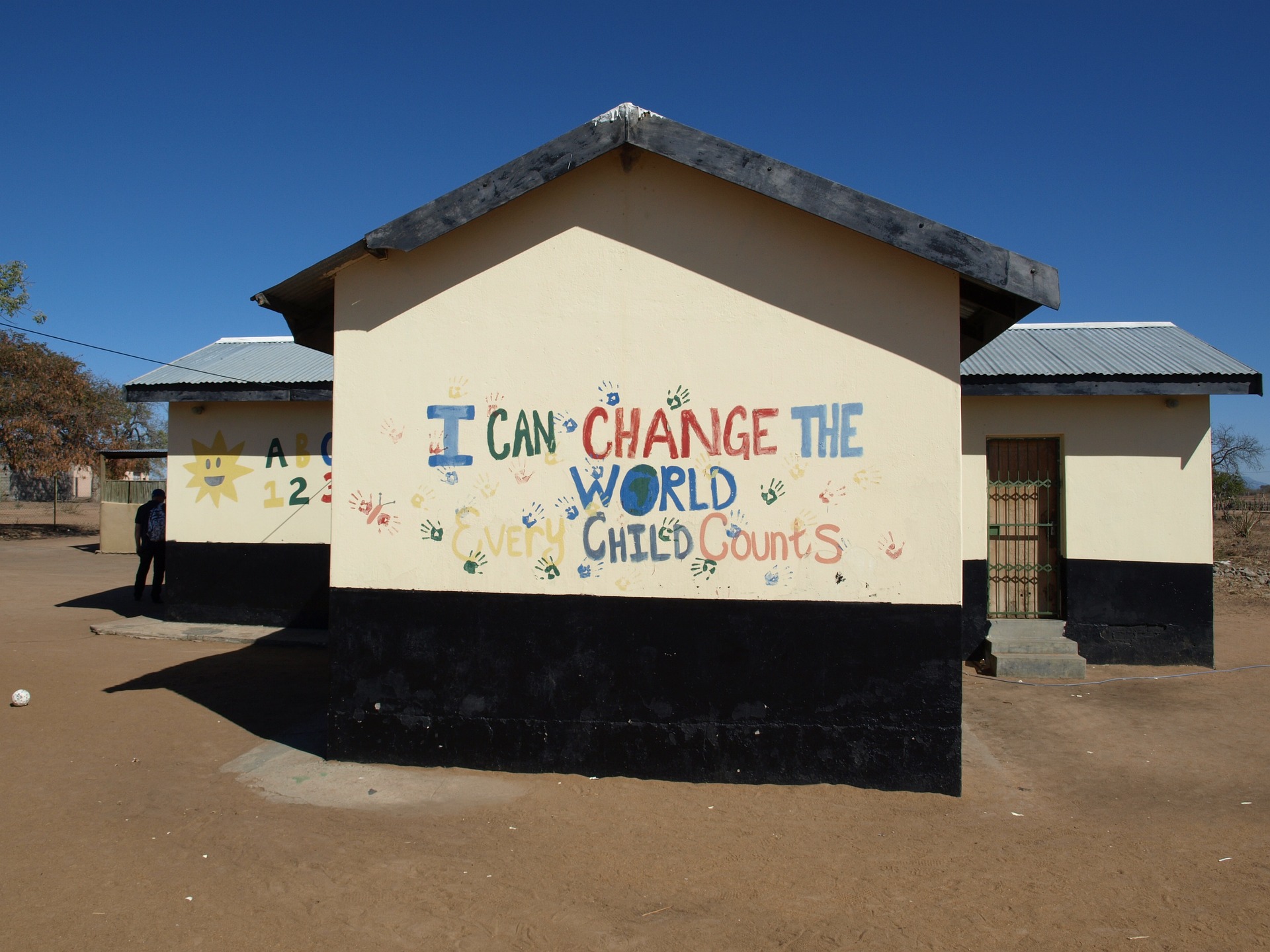 Image of school building against blue sky with colourful handprints and painted letters reading 'I can change the world every child counts'