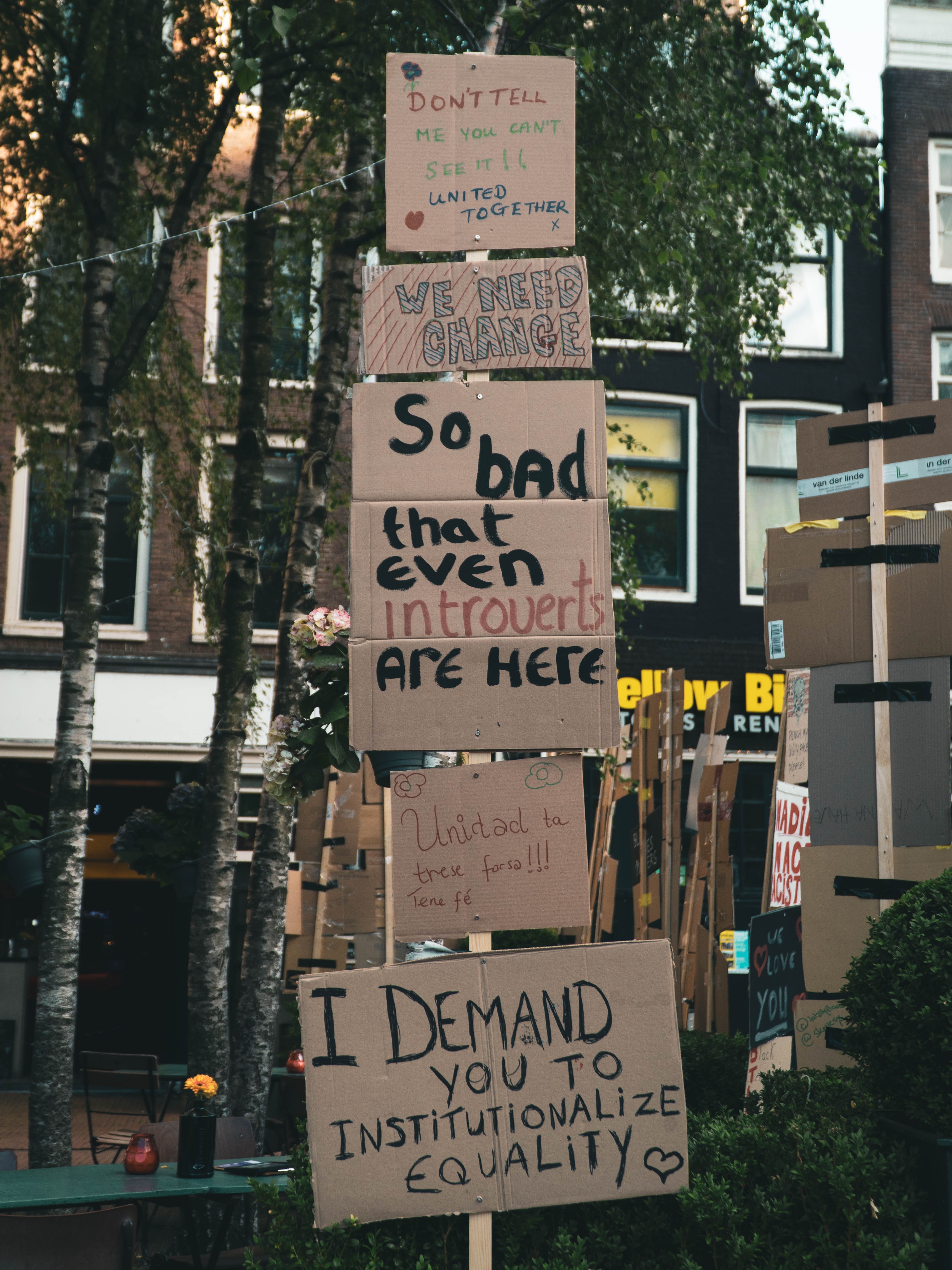 Photo showing series of placards in a stack in what appears to be a square or plaza. The bottom one reads 'I demand you to institutionalise equality'